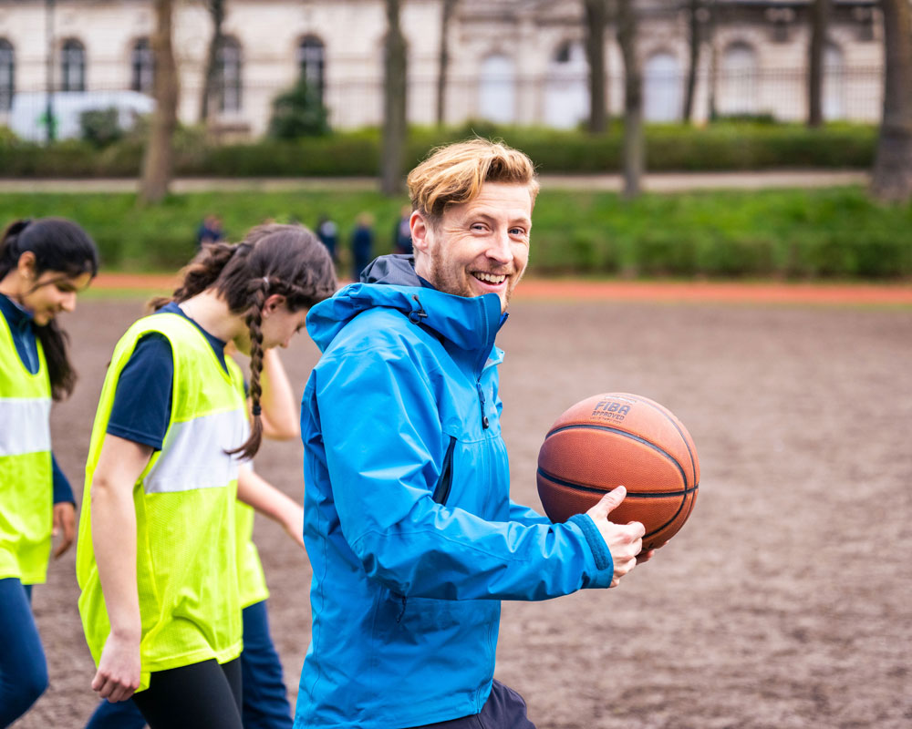 A BJAB teacher carrying a basketball during an outdoor games session on the sports ground